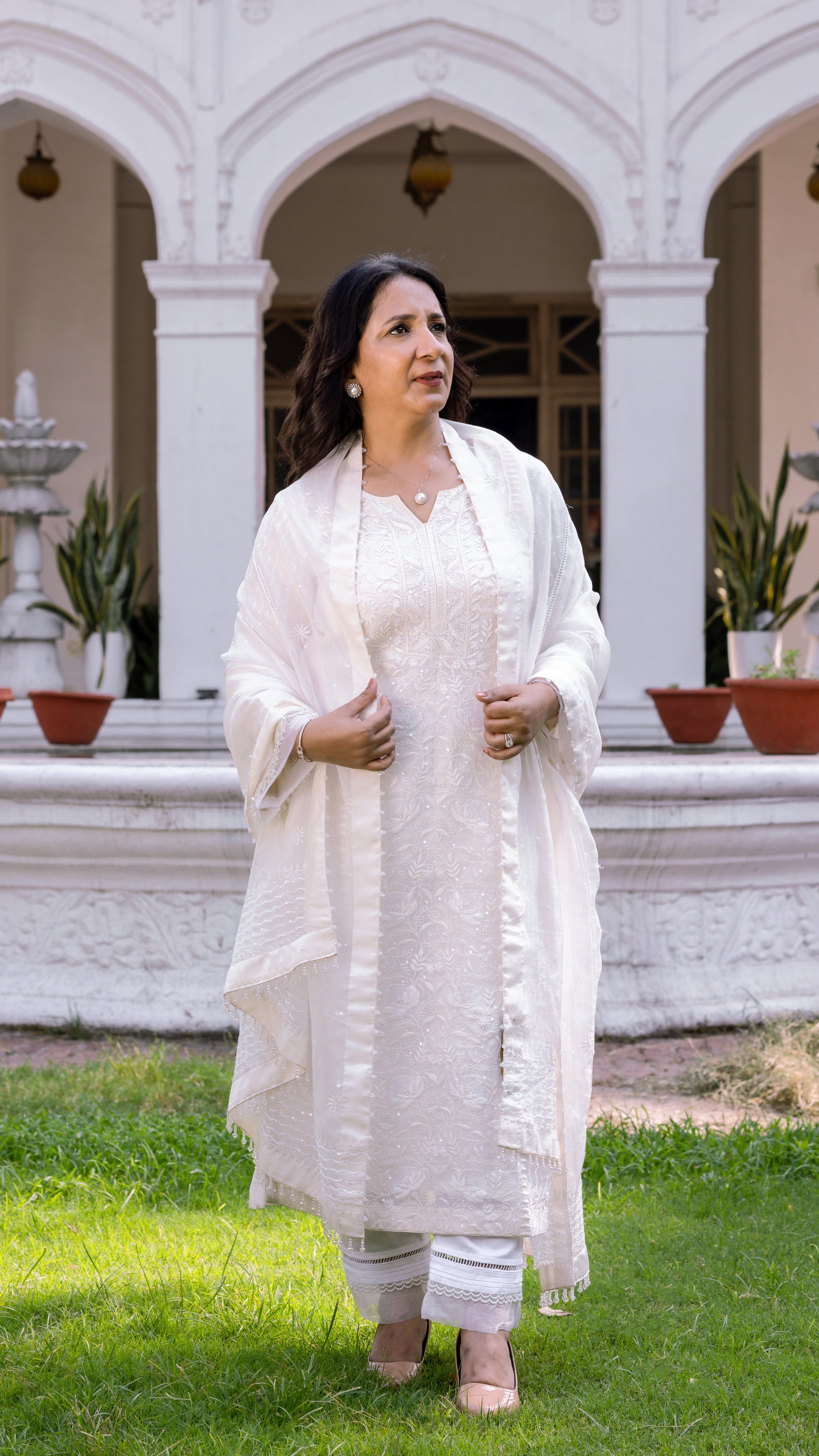 Woman in a white traditional outfit standing in front of a white building with arched windows.